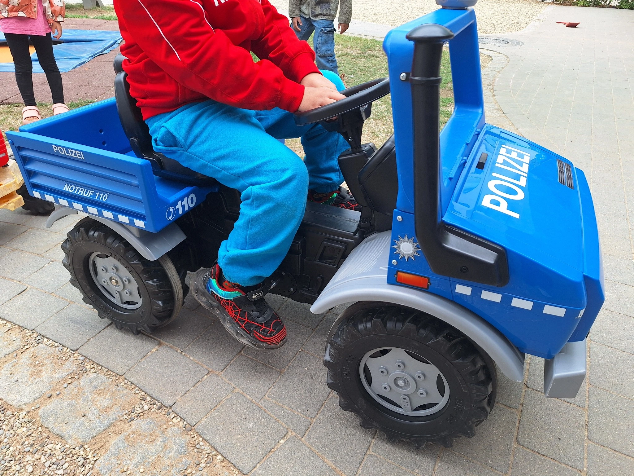 Ein Kind fährt im neuen blauen Spielzeug-Polizeiauto des Kinderhauses Luise Scheppler